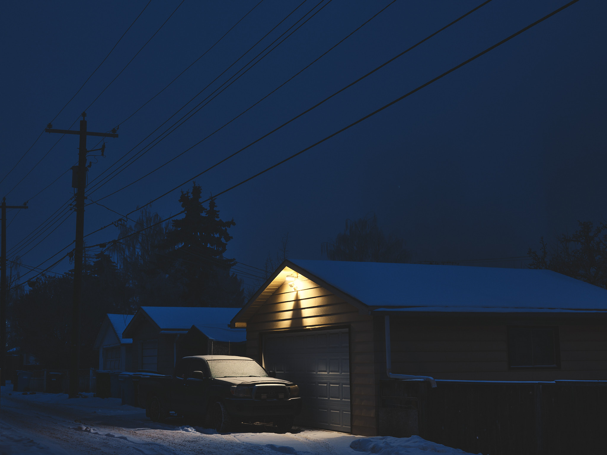 Garage and snow-covered truck in deep blue hour winter night