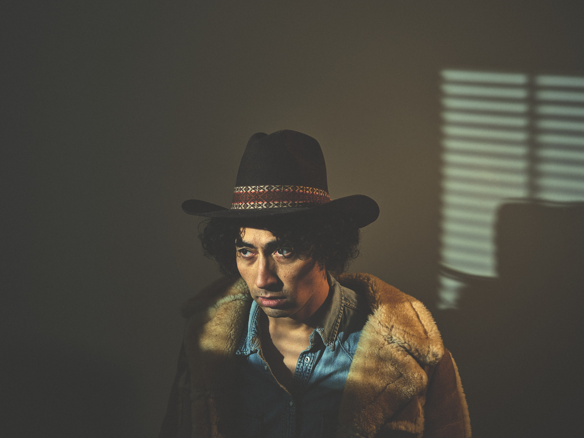 Cowboy portrait with patterned hat band, denim and sheepskin, window light