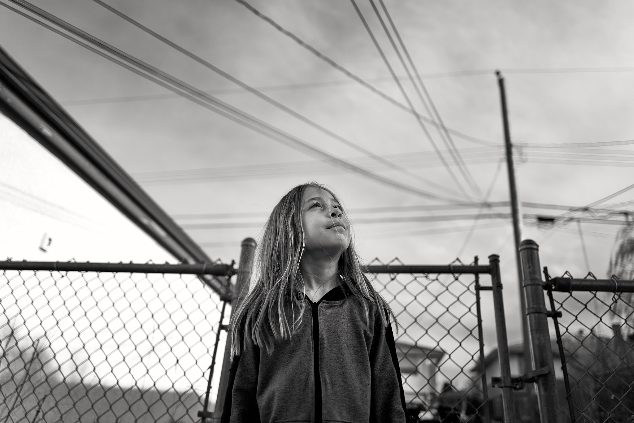 Young person looking upward against chain-link fence and power lines, black and white
