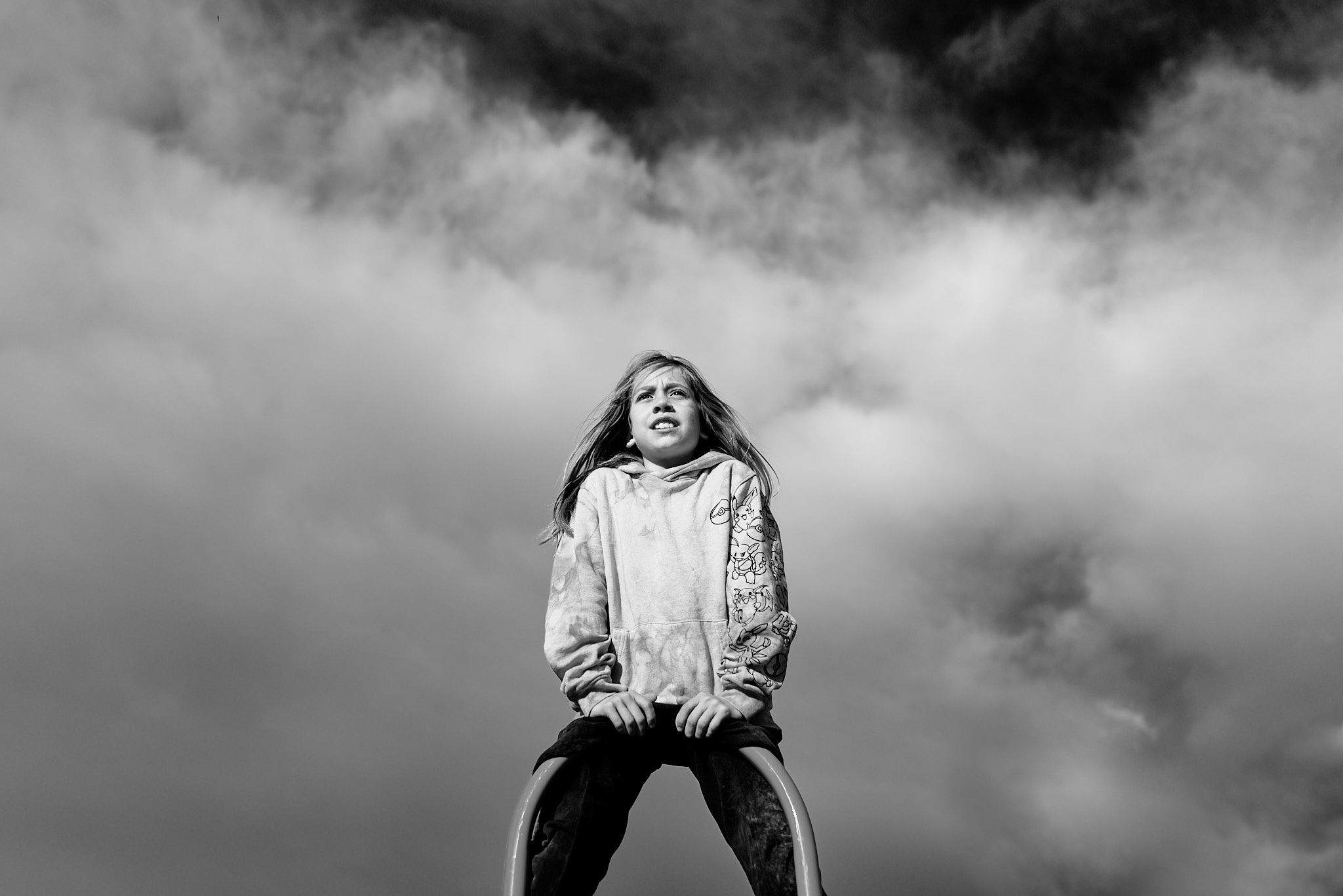 Child sitting atop playground equipment against dramatic prairie clouds, black and white