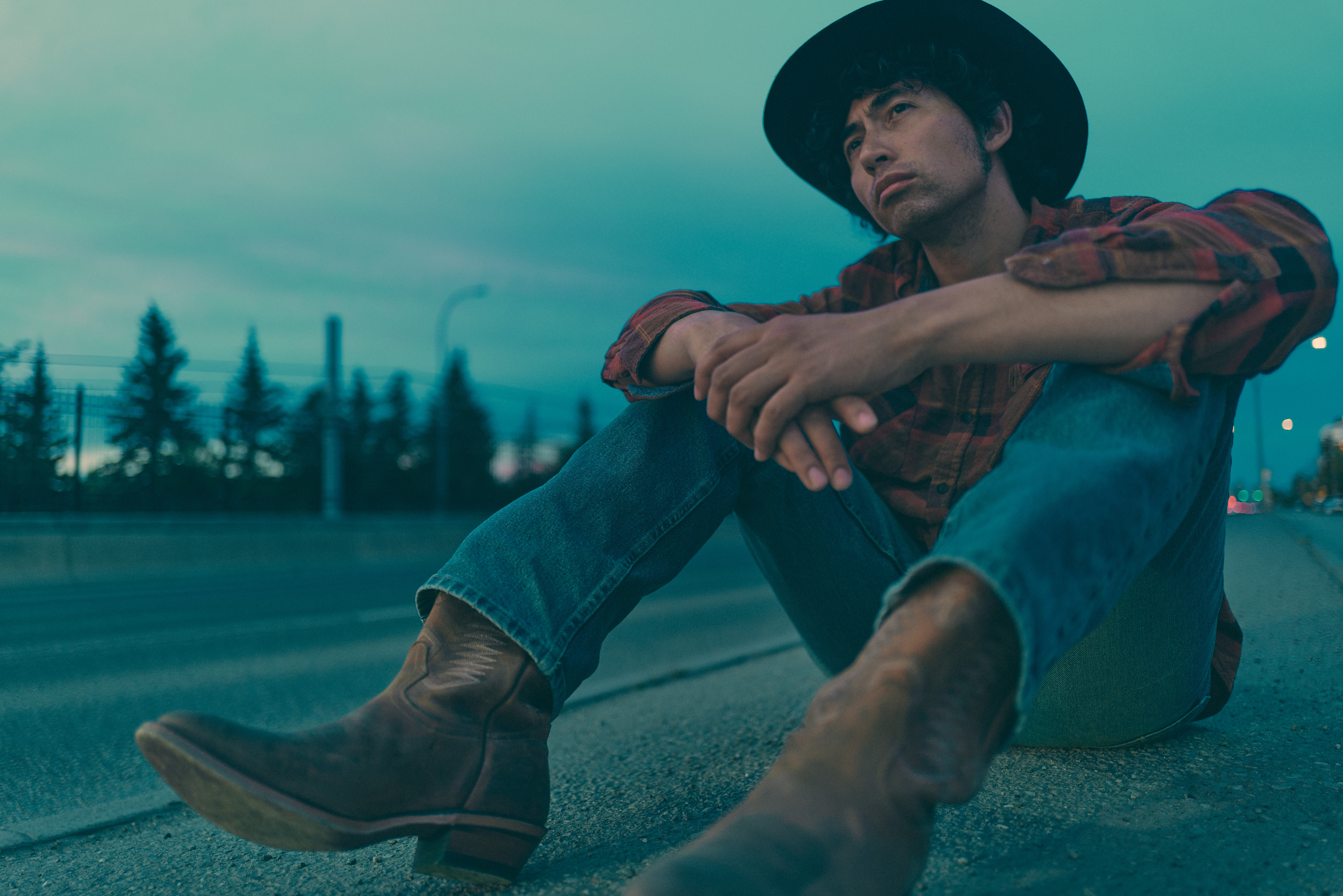 Cowboy sitting on a road at dusk, boots and hat, blue hour light