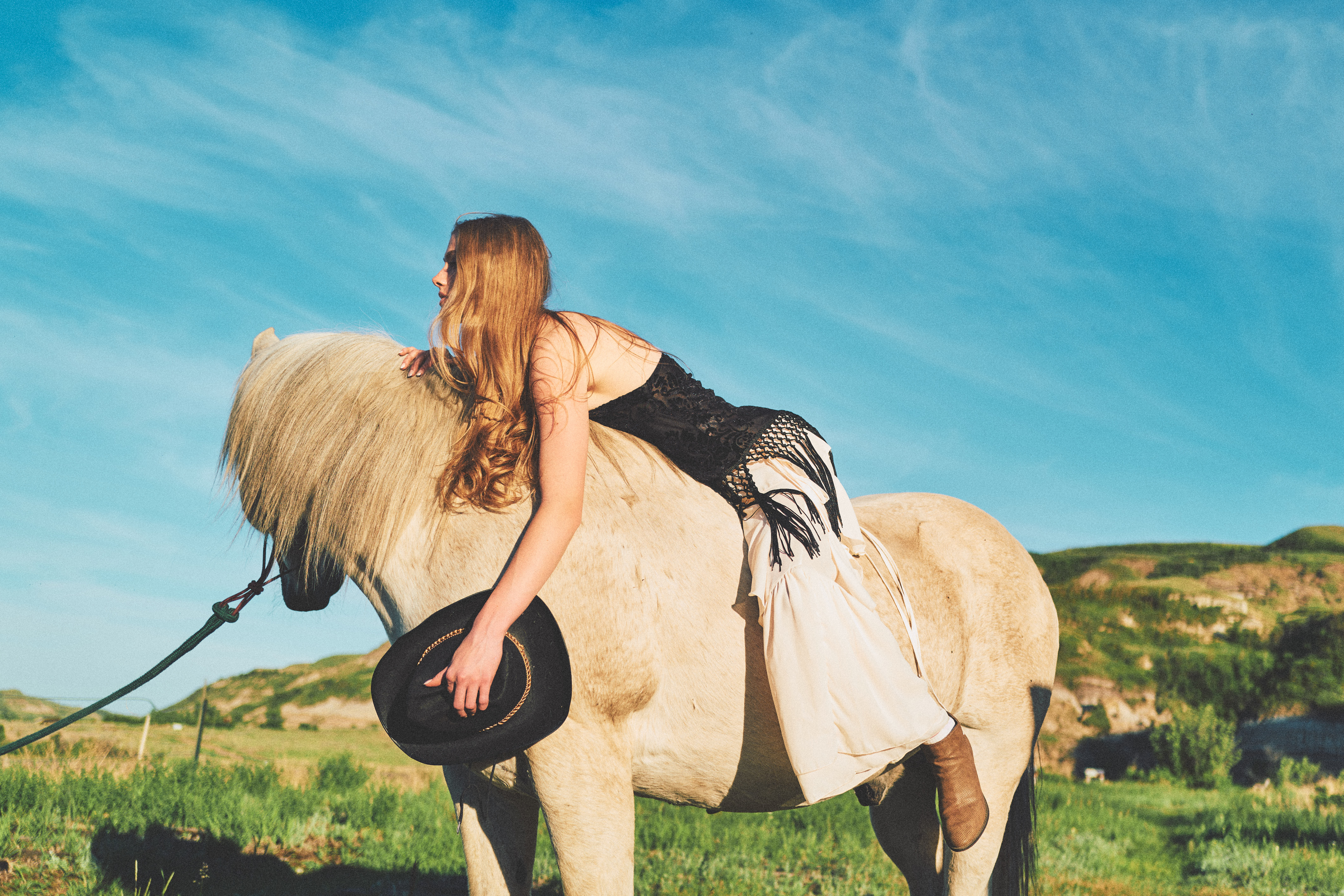 Woman draped over palomino horse holding cowboy hat, golden hour in the Alberta badlands