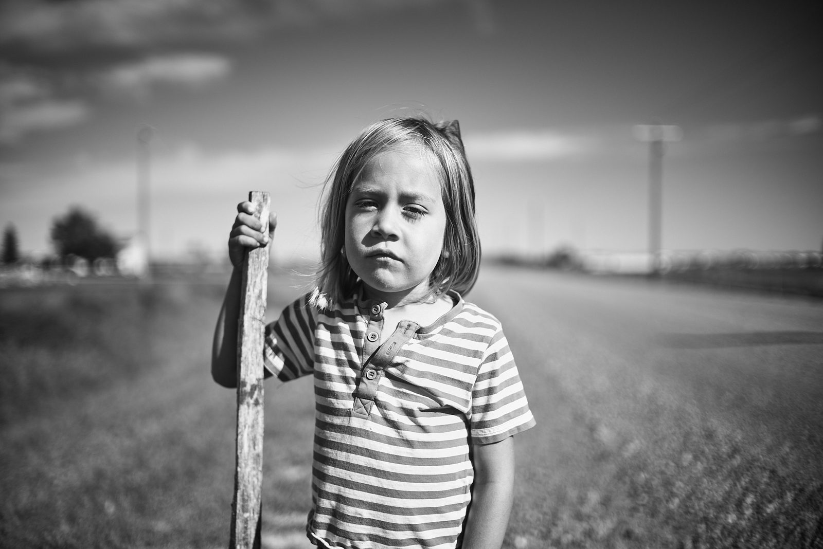 Child holding stick by prairie road — black and white portrait photography Alberta