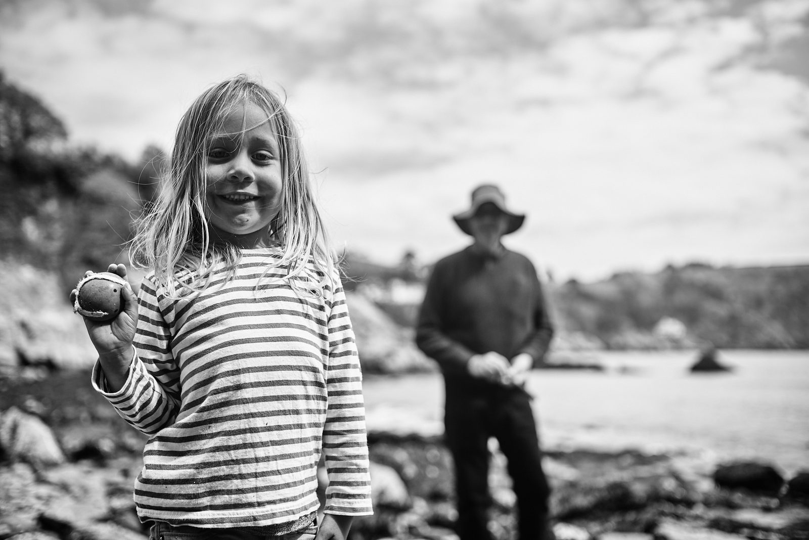 Child holding pebble on rocky coast with father — black and white portrait photography