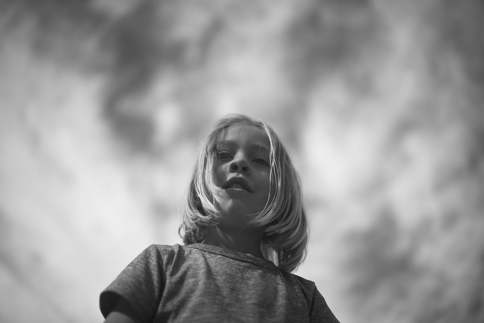 Child portrait from low angle with dramatic clouds — black and white portrait photography