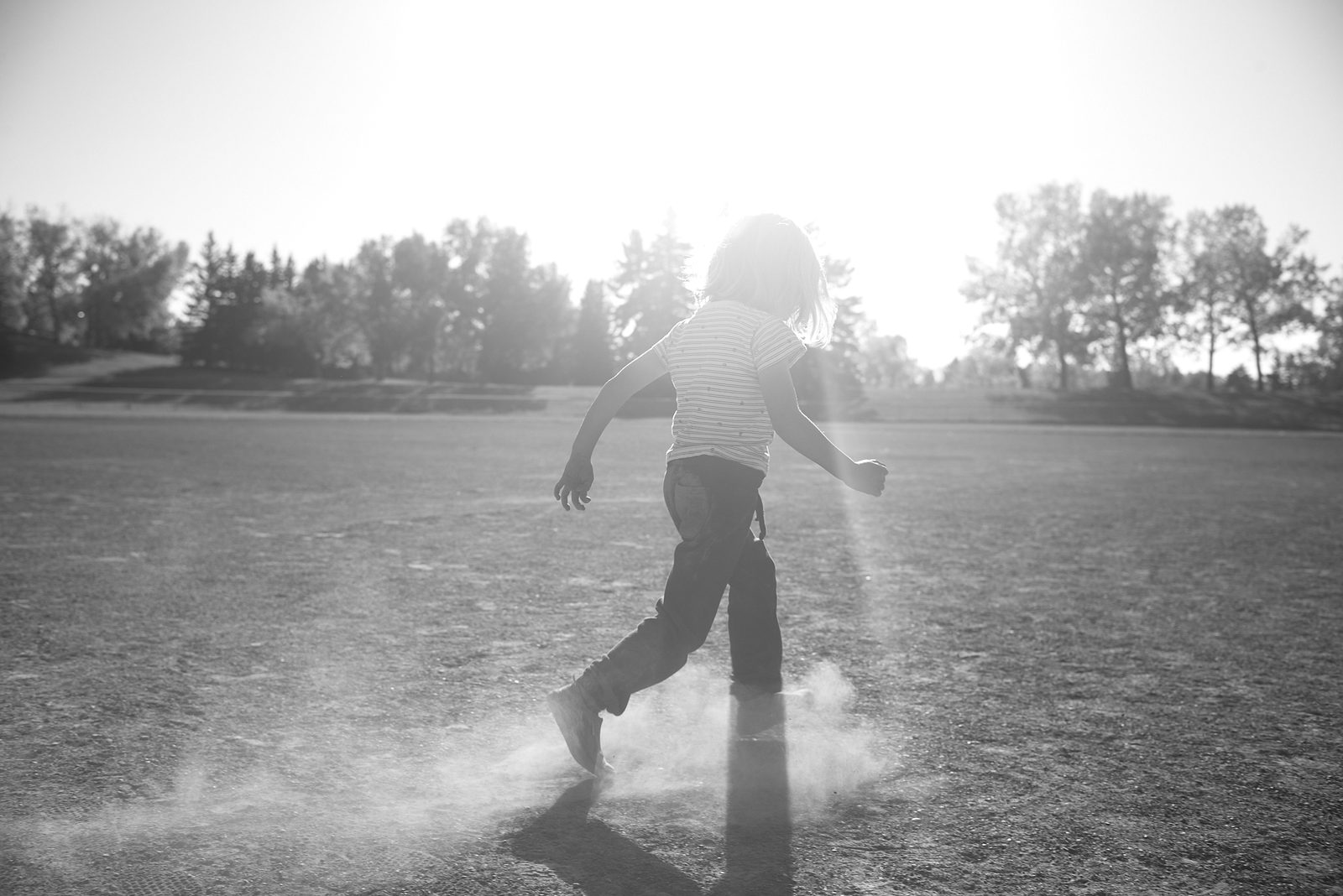 Child running through dust in backlit field — black and white fine art photography