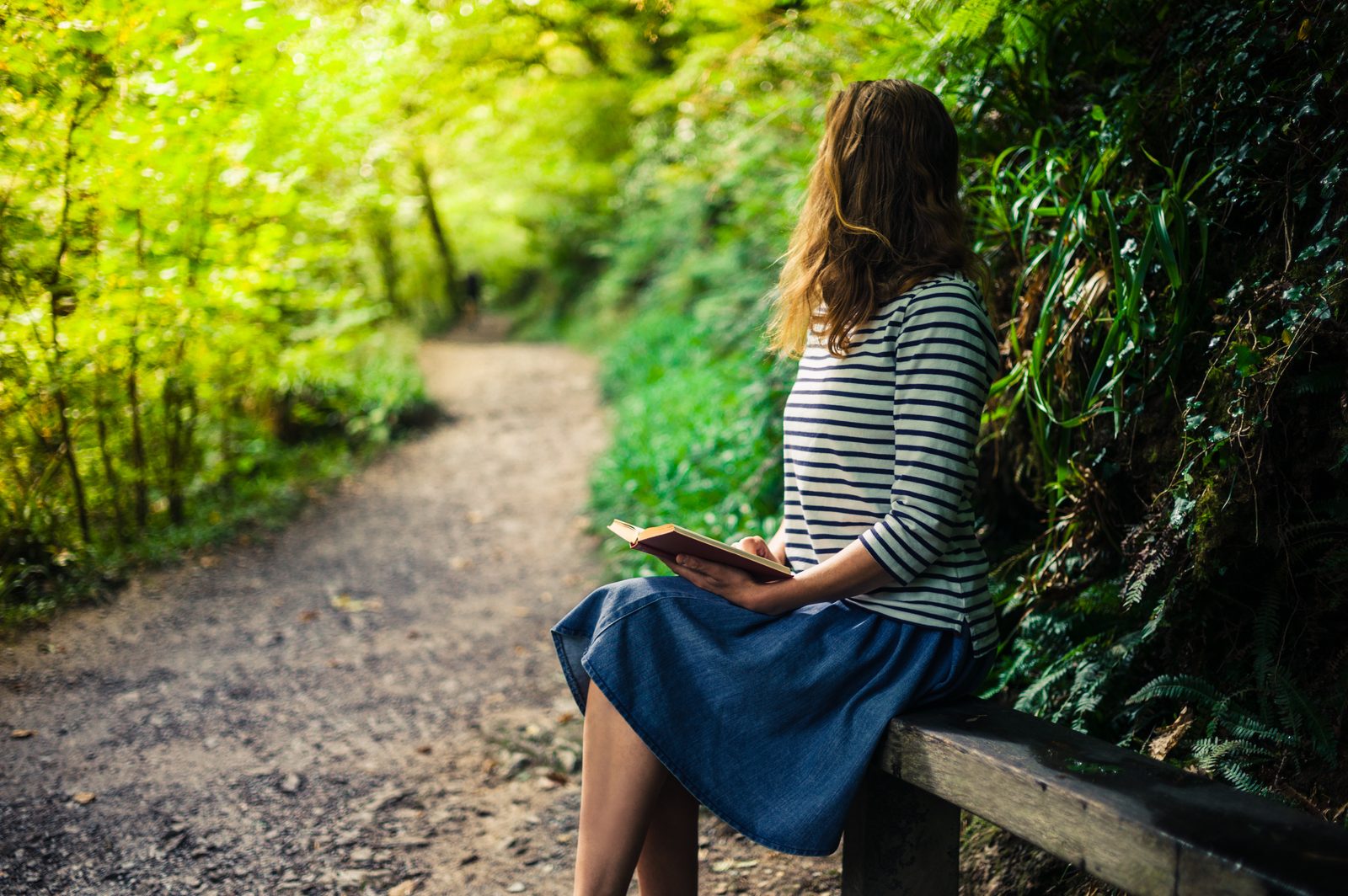 Woman reading on bench in green forest — natural light lifestyle photography