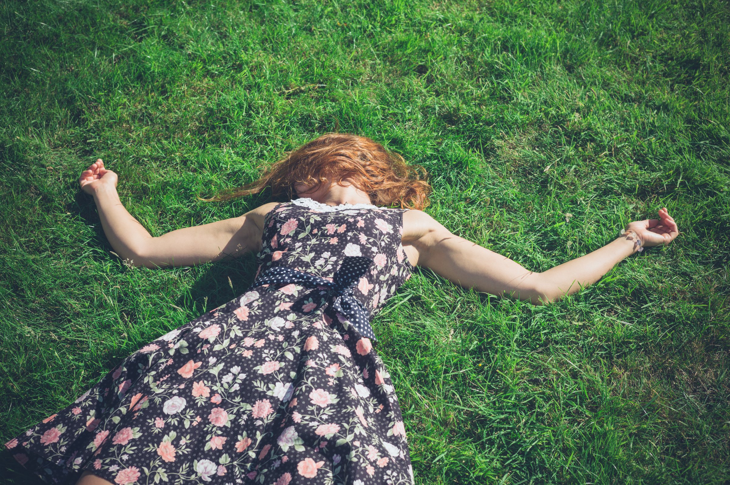 Woman in vintage floral dress lying in summer grass, red hair fanned out